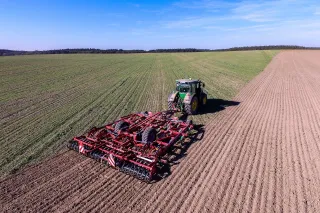 Traktor s červeným kultivátorem Kverneland při práci na poli