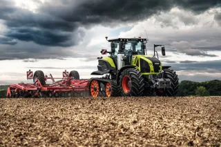 Zelený pásový traktor Claas Axion Terra Trac s červeným strojem na zpracování půdy