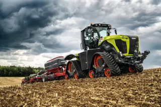 Zelený pásový traktor Claas Xerion se secím strojem na poli