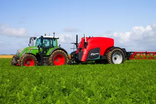 Zelený traktor Fendt s červeným taženým postřikovačem Kverneland iXtrack T6 na poli