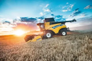 Žlutá sklízecí mlátička New Holland CR při západu slunce