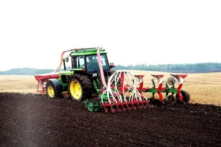 Zelený traktor s pluhem a secím zařízením Kverneland na poli
