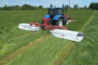 Žací stroj Kuhn GMD 8730 za modrým traktorem na louce