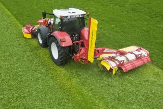 Červený traktor se žacím strojem Pöttinger na poli