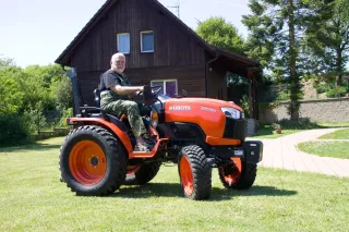 Muž řídí oranžový malotraktor Kubota před domem