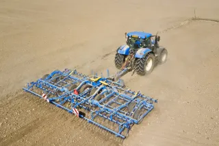 Modrý traktor táhne kypřič Farmet po poli