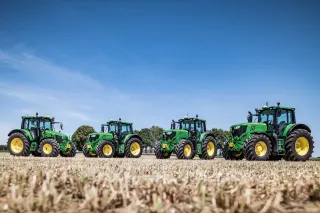 Tři zelené traktory John Deere na poli