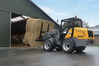 Nakladač Giant manipuluje s balíky sena u haly