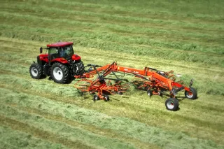 Červený traktor se shrnovačem Kuhn na louce