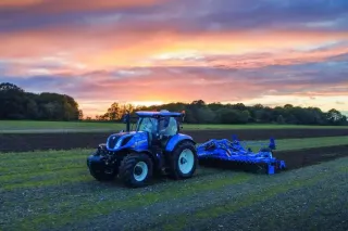 Traktor New Holland na poli při západu slunce