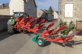 Traktor s pluhem Kverneland před venkovskými domy