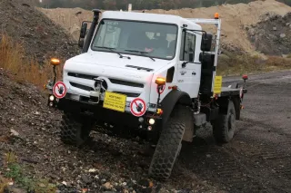 Bílý vůz Mercedes-Benz Unimog v terénu