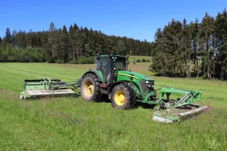 Traktor John Deere se žacím strojem na louce