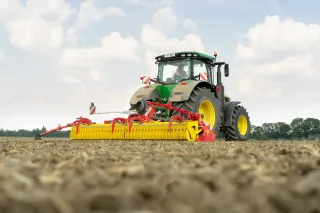 Traktor s rotačními branami Pöttinger na poli
