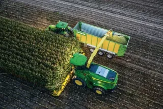 Řezačka John Deere a traktor synchronizovaně při sklizni kukuřice