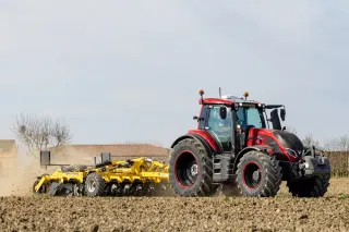 Červený traktor Valtra s půdním nářadím na poli