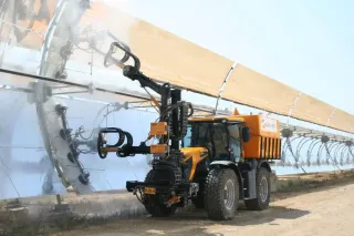 Oranžové vozidlo s rameny čistí odrazové panely solární elektrárny
