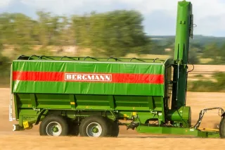 Zelený překládací vůz Bergmann zapřažený za traktor při sklizni