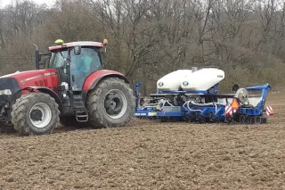 Červený traktor Case IH se secím strojem Kinze 3500 při setí na poli