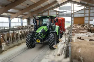 Traktor Deutz-Fahr s krmným vozem projíždí stájí s dobytkem