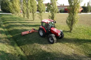 Červený traktor McCormick X5.085 s bočním žacím strojem na louce