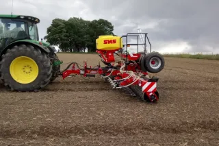 Zelený traktor se secím strojem SMS na poli