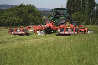 Traktor s červenou žací kombinací Kuhn FC 9330 RA při sečení louky