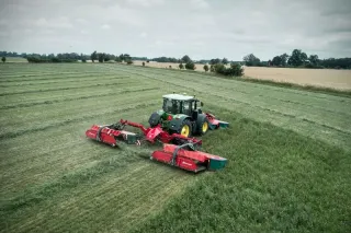 Traktor s červenou žací trojkombinací Kverneland na louce
