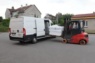 Vysokozdvižný vozík nakládá materiální pomoc do bílé dodávky