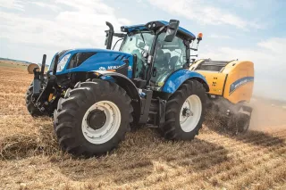 Modrý traktor New Holland s lisem na slámu při práci na poli