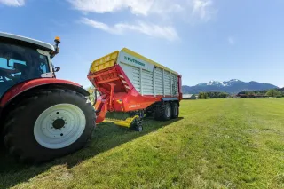 Traktor táhne sběrací vůz Pöttinger Jumbo na louce