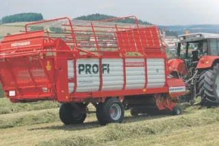 Červený sběrací vůz Pöttinger Profi tažený traktorem při senážování