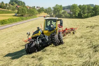 Žlutý traktor Rigitrac s obracečem píce na horské louce