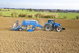 Modrý traktor se secím strojem Farmet Falcon při práci na poli