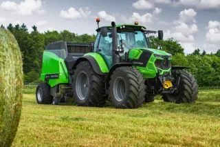 Zelený traktor Deutz-Fahr s lisem na louce