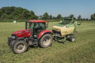 Červený traktor Case IH táhne lis Krone na louce