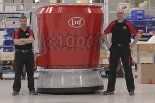 Dva pracovníci stojí vedle jubilejního krmného robota Lely Vector
