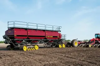 Velký červený secí stroj Seed Hawk tažený traktorem na poli