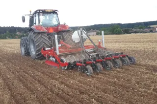 Červený traktor táhne podmítač SUMO TRIO po poli