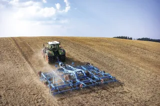 Traktor Fendt táhne modrý kypřič Lemken Koralin po strništi.