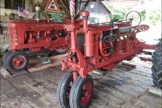 Historické červené traktory Farmall v dřevěné hale.