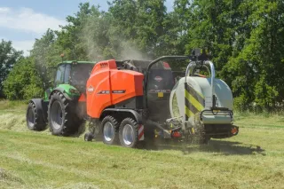 Traktor s lisem Kuhn a ovíječkou balíků na louce