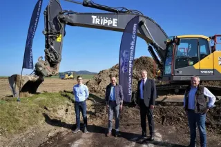 Čtyři muži stojí před pásovým rypadlem na staveništi