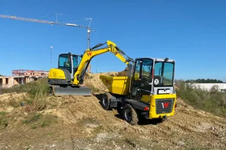 Žluté rypadlo nakládá zeminu do dampru Wacker Neuson