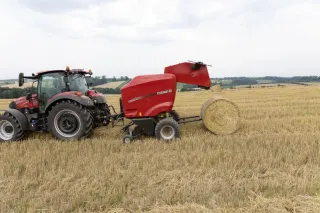 Červený lis Case IH tvoří kulatý balík slámy na poli.
