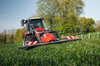 Červený traktor Massey Ferguson s čelním žacím strojem na louce.