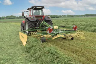 Traktor s jednorotorovým shrnovačem Krone Swadro na posečené louce.