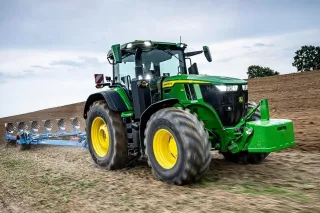 Zelený traktor John Deere s pluhem na poli.