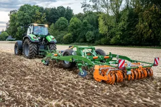 Traktor táhne zelený a oranžový kombinovaný kypřič Amazone Ceus po strništi.