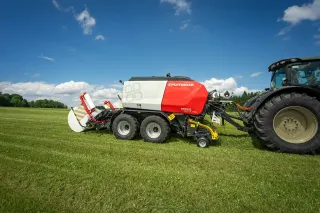 Kombinovaný lis Pöttinger Impress připojený k traktoru na louce.